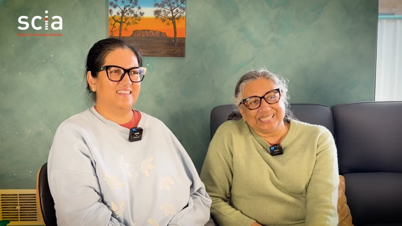 Poonam Shah seated to the left and her mother Chandrika seated to the right. They are in a home setting with artwork hanging behind them.