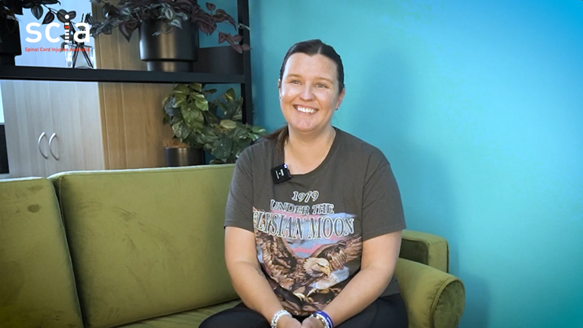 Elizabeth is smiling and seated on a green lounge against a teal wall.