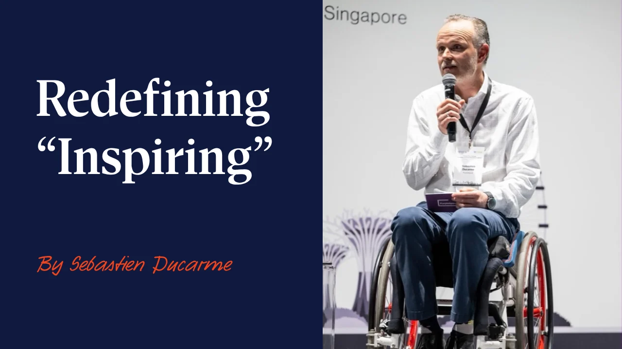 Seb, seated in his wheelchair, speaking on stage at a disability-inclusive business event in Singapore, 2025.